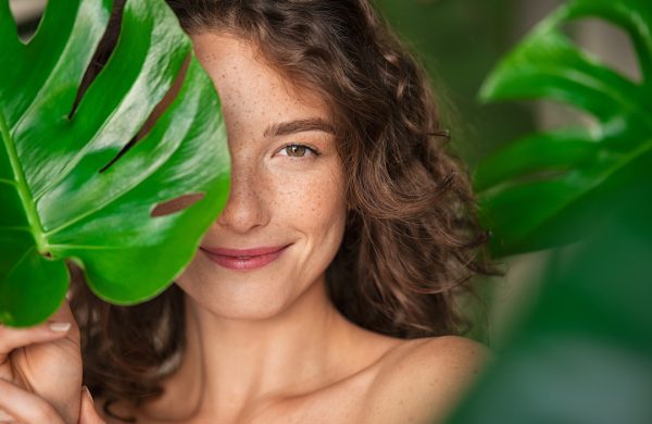 close de rosto de mulher sorridente segurando folha para ilustrar texto sobre marcas de cosmético sustentáveis